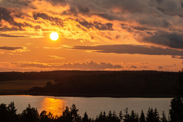 The orange setting sun with dramatic clouds above a lake.