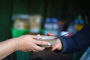 A handover of a bowl with spoon between two persons