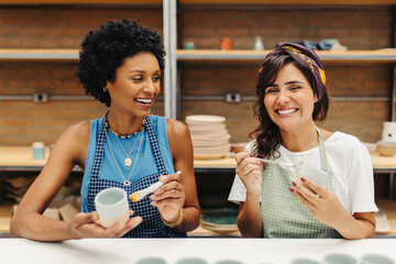 Happy female ceramists decorating their handmade ceramic cups