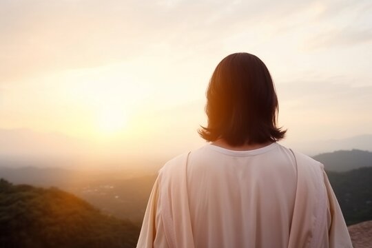 Back view of Jesus Christ looking at a sunset, praying to God, praying for us