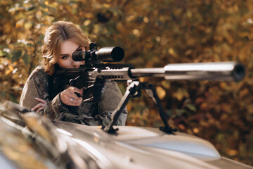 A female soldier fires a rifle from the hood of a pickup truck. War, army, military concept.