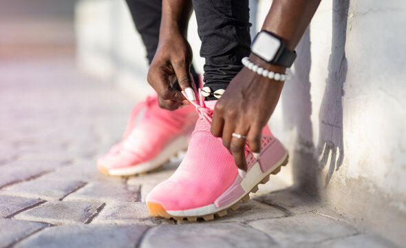 Closeup of young black woman's hands wearing a smartwatch tying the laces of her running shoes, getting ready for a jog on the road.