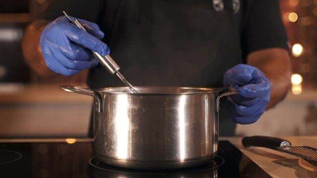 Close up of a chef man hands in gloves whisking in a stainless steel pot in the kitchen. Cooking tasty hot chocolate