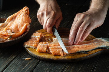 Cutting red fish on a kitchen cutting board before salting. Cook's hands with a knife while cleaning pink salmon. The idea of a fish diet.