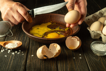 The cook prepares eggs on the kitchen table for an omelette. The chef hands hold a knife to break an egg. Healthy egg diet