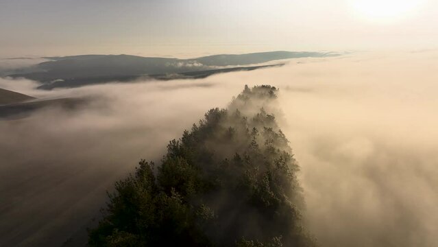 An aerial view of the mist creeping over the hills. Rapid movement of fog or steam over the ground in the early morning or evening at sunset. Weather change peace and tranquility