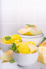 Homemade melon ice cream balls in portioned bowls, with slices of fresh cantalupa melon and mint leaves