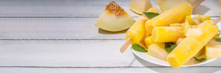

 Melon ice cream popsicle, sweet sorbet lollypops, homemade gelato on sticks, with slices of fresh cantalupa melon and mint leaves  - obrazy, fototapety, plakaty