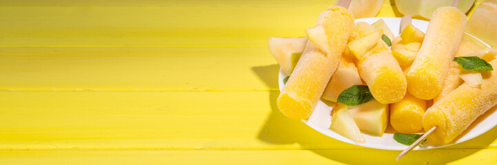 

 Melon ice cream popsicle, sweet sorbet lollypops, homemade gelato on sticks, with slices of fresh cantalupa melon and mint leaves 