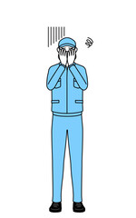 落ち込んで顔を覆う帽子と作業着姿の男性