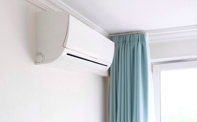 Modern air conditioner on white wall indoors. Hand with remote control directed on air conditioner.
