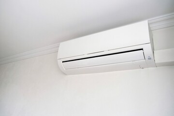 Modern air conditioner on white wall indoors. Hand with remote control directed on air conditioner.