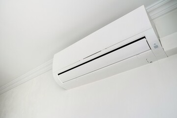 Modern air conditioner on white wall indoors. Hand with remote control directed on air conditioner.