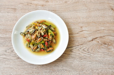 spicy stir fried mussel with slice onion and basil leaf on plate