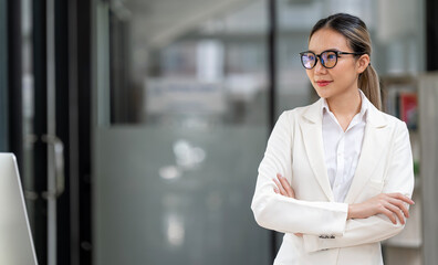 Happy relaxed confident young businesswoman standing with folded arms in office looking away with a warm friendly smile