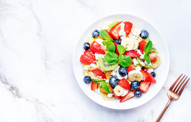 Summer fruit and berry salad with cottage cheese and mint leaves with honey dressing, marble table background, top view
