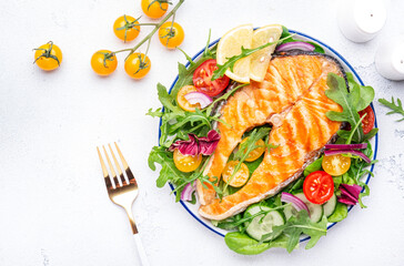 Grilled salmon steak with vegetable salad with tomatoes, arugula, onion  and lettuce on plate, gray table background, top view