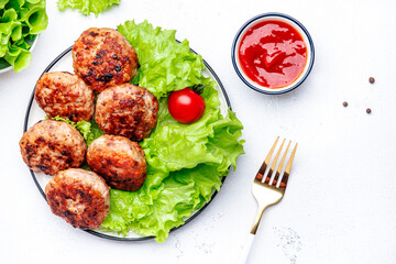 Homemade fried pork and beef meatballs with green lettuce and tomatoes, white table background, top view