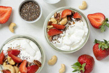 Greek yogurt, nuts and strawberries in a glass jars on a white table top view