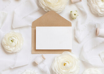 Obraz na płótnie Canvas Blank card and envelope near cream roses and white ribbons top view, wedding mockup