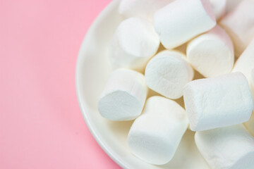 Plate with vanilla marshmallows on a pink background.