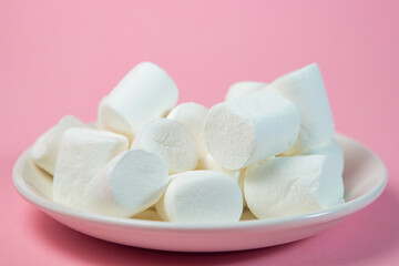 Plate with vanilla marshmallows on a pink background.