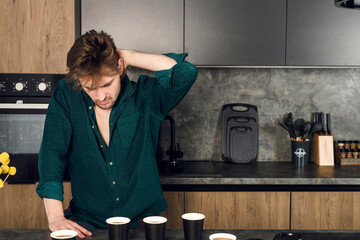 Sleepy man addicted to coffee cant stop drinking in the kitchen, many cups scattered around a table. caffeine addiction concept. - obrazy, fototapety, plakaty