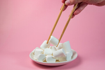 Chopsticks are tearing marshmallows on a pink background