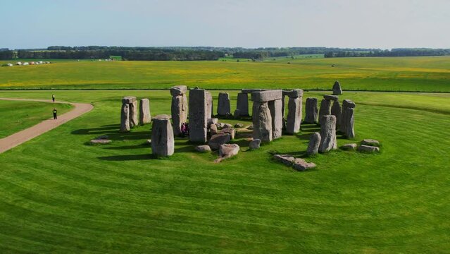 Drone aerial shot orbiting Stonehenge on a sunny day with tourists