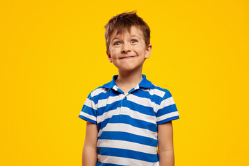 Surprised kid boy wearing blue striped polo, makes funny grimace, isolated over yellow background.