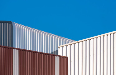 Fototapeta premium Corrugated metal industrial office buildings with aluminum warehouse against blue clear sky Background