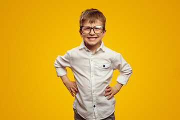 Little nerd kid wearing glasses and white shirt smiling for camera while keeping hands on waist...