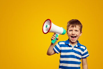 Excited kid leader speaking in megaphone and smiling while standing against yellow background with...