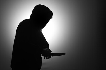 Mysterious man wearing black hoodie holding a knife to stab someone. Crimes and criminality concept