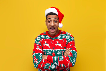 young guy in New Year's clothes and santa hat is surprised and shouts on yellow isolated background