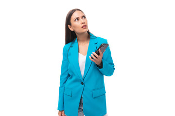 young brunette model woman dressed in a stylish business jacket thoughtfully holding a smartphone...