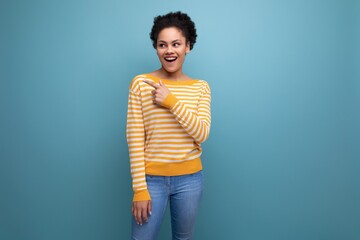 smiling latin young woman with afro hair in a yellow sweater points with a finger for an idea