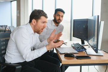 Two men traders sitting at desk at office together looking at data analysis discussing brainstorming successful strategy inspired teamwork concept close-up