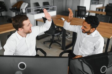 Two successful trader sitting in office and looking at screen, checking cryptocurrency information data on finance market graph, pointing on monitor