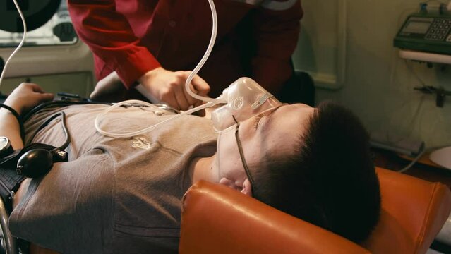 An EMS paramedic team provides medical care to an injured patient. A male emergency room attendant performs resuscitation to stabilize the vital organs of a man in an ambulance.