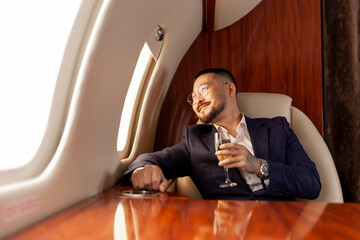 asian businessman in suit and glasses with glass of champagne flies in private luxury jet, korean...