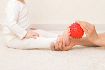 Masseur hand holding red massage ball and massaging infant foot on carpet. Baby healthcare....