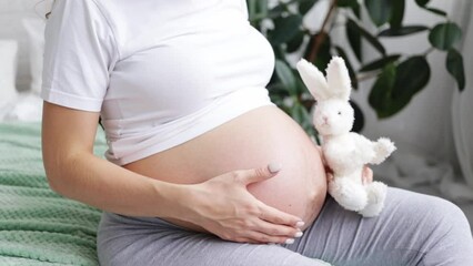 hands close-up of a pregnant girl with a big belly at the last term gently stroking his hands and dreaming of the birth of a baby in a bright bedroom, slow motion video.