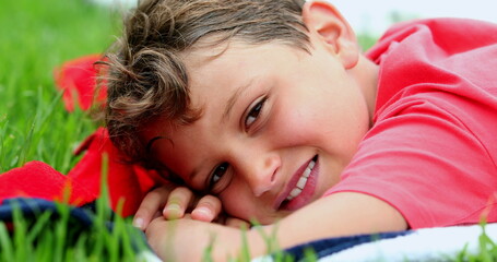 Handsome young boy smiling to camera laid on grass outside