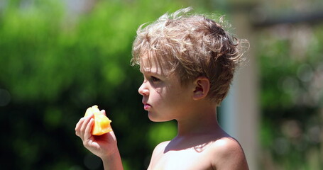 Handsome toddler child holding and eating yellow melon fruit