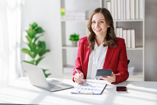 Concept of business office woman working,Businesswoman smile while working about her invesment plan with analyzing document and business investment graph data by using laptop on desk in workstation.
