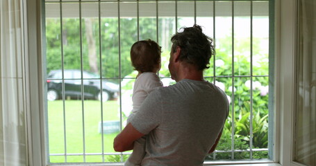 Grandparent holding grandson baby next to window during summer day
