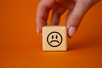 Sad smile symbol. Sad smile on wooden cube. Businessman hand. Beautiful orange background. Business and Sad smile concept. Copy space.