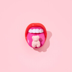 Red mouth with tongue sticking out, gummy bear on it, creative pop art layout, candy pink background. 