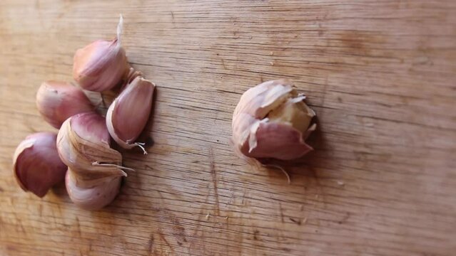 the art of garlic crushing as a stainless steel knife expertly flattens garlic cloves using the edge of the blade on a rustic wooden cutting board. 